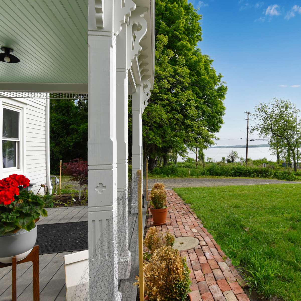 A view from a porch with a brick pathway leading to a grassy area and a lake visible in the distance, framed by trees.