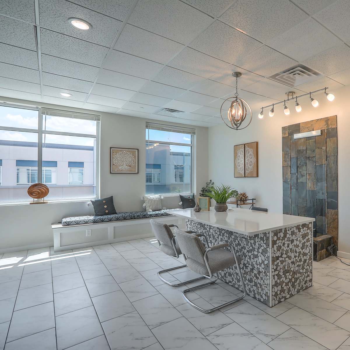 A modern office waiting area featuring a stone accent wall, a white reception desk, seating along the windows, and decorative artwork.