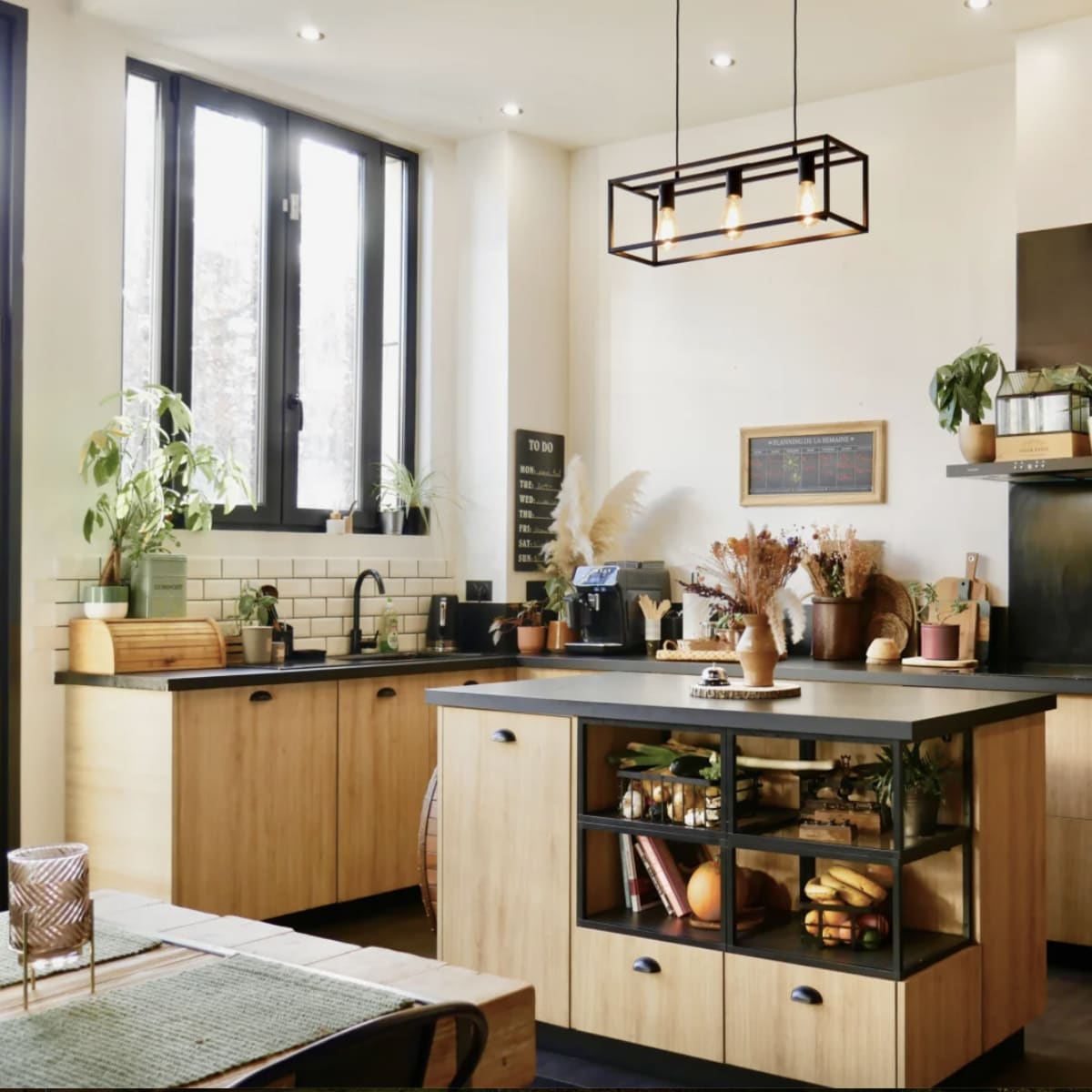 A modern kitchen features wooden cabinetry, an island with a glass front displaying fruits, and various kitchen appliances against a light backdrop.