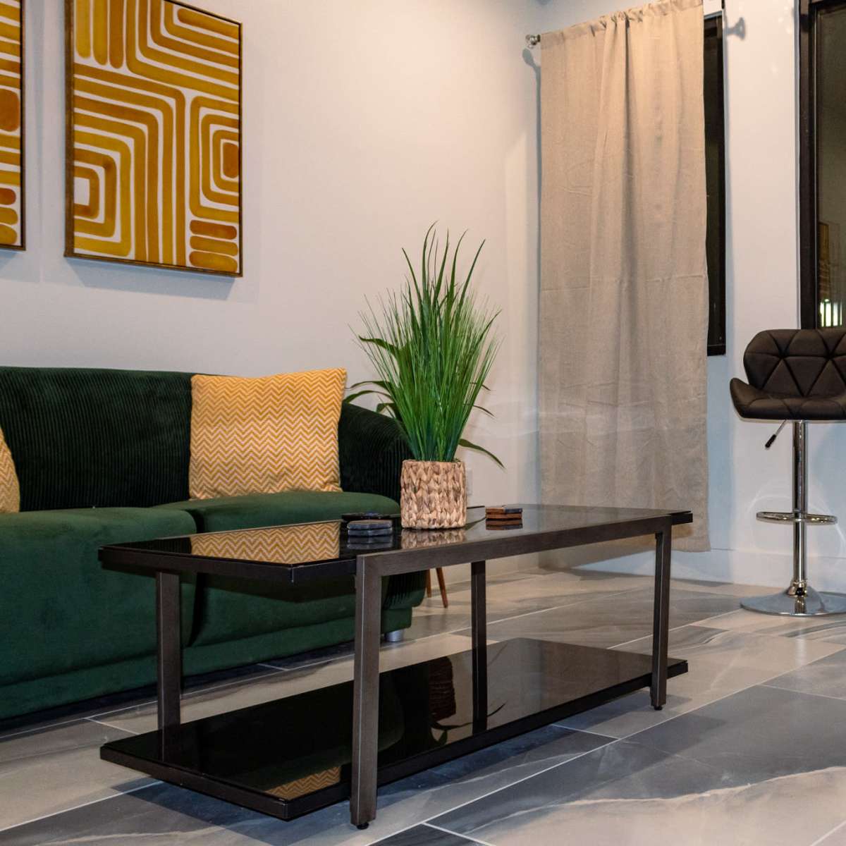 A modern living space with a green sofa, a coffee table, and two bar stools near a window.