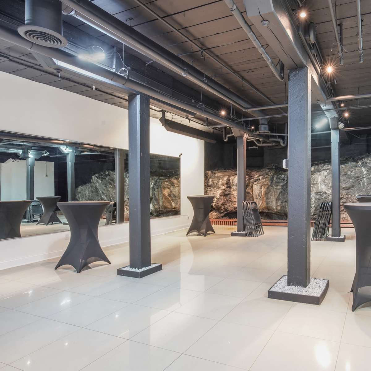 A spacious venue with dark columns and sleek tables, featuring a rock wall in the background.