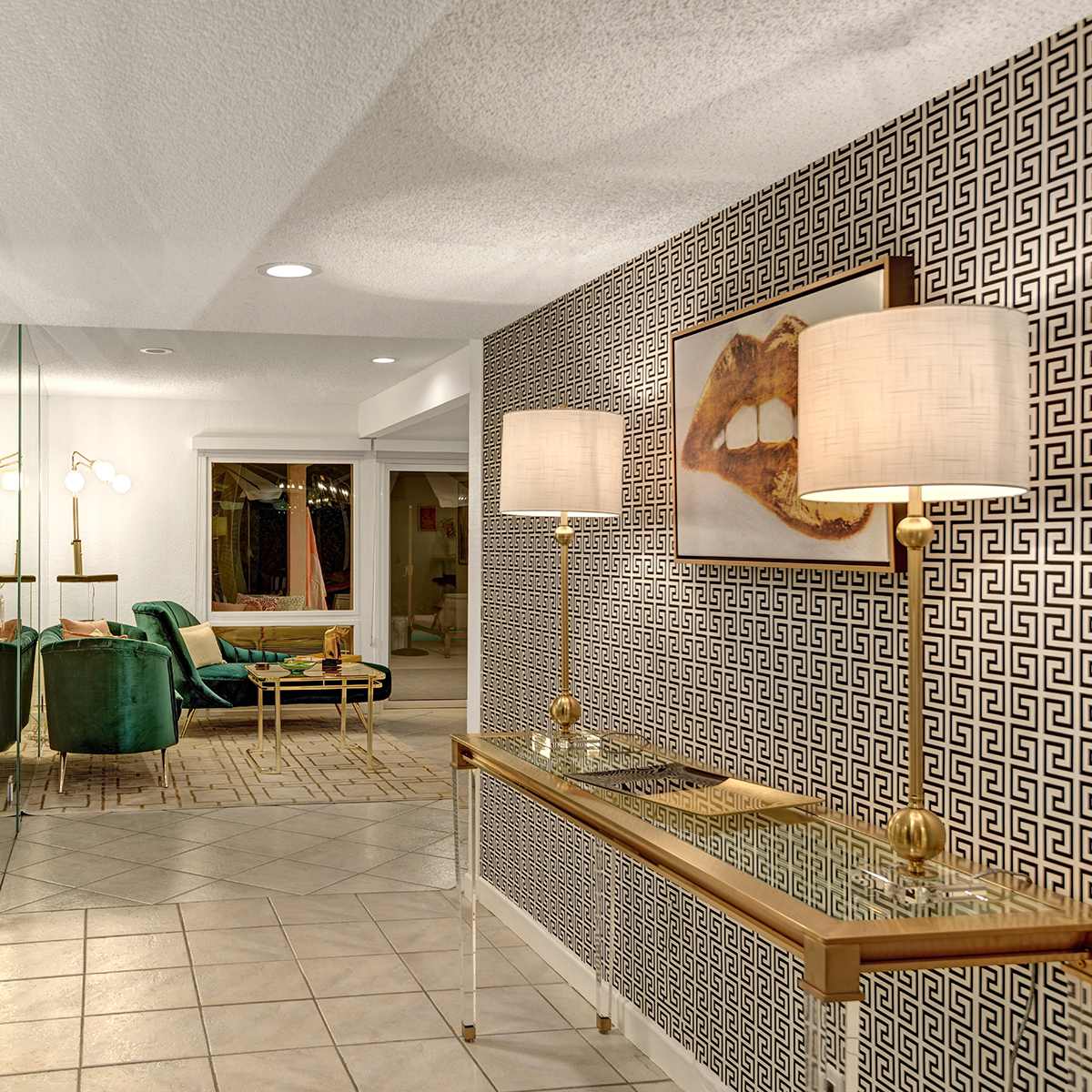 A modern entryway features a decorative wall with a geometric pattern, a console table with a glass top, and green chairs visible in the background.