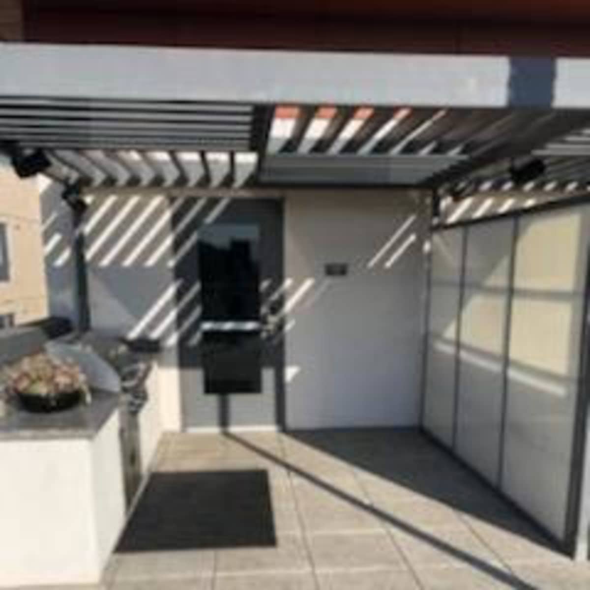 An outdoor area with a grill, a paved floor, and a door under a striped awning.