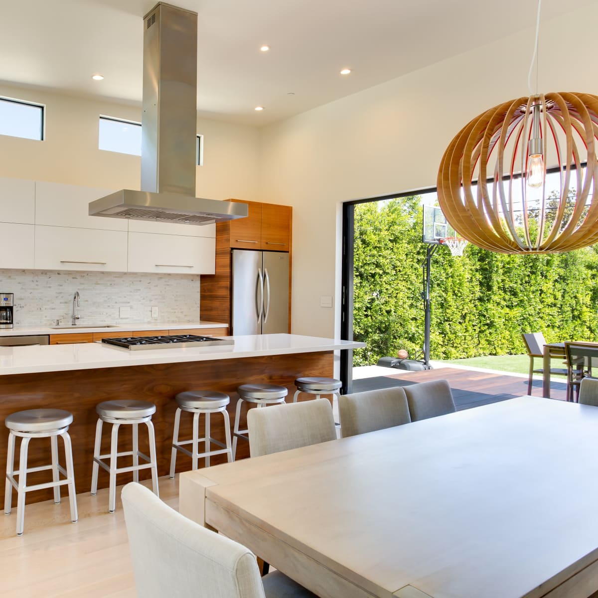 A modern kitchen with a central island, sleek cabinetry, and a dining area that opens to an outdoor view.