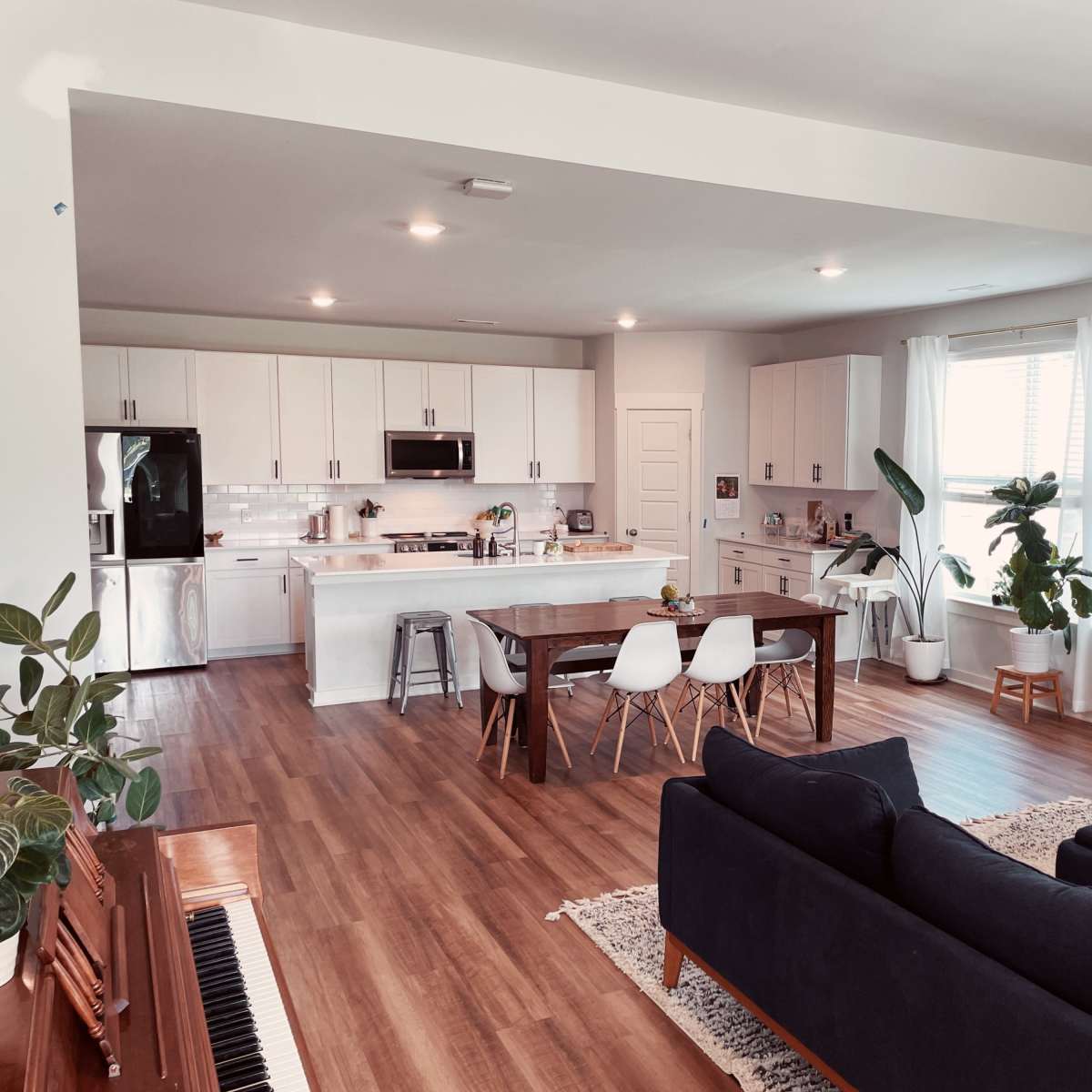 A modern open-concept kitchen and dining area with a wooden table, white chairs, and a sofa in a well-lit space.
