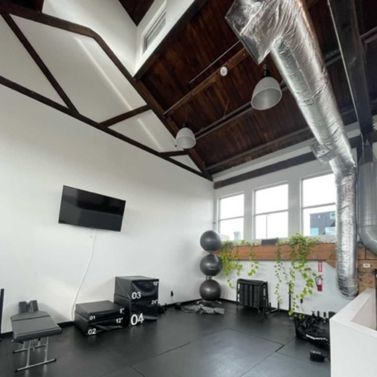 A workout space with black rubber flooring, a wall-mounted television, a weight bench, and various fitness equipment, including exercise boxes and a large stability ball.