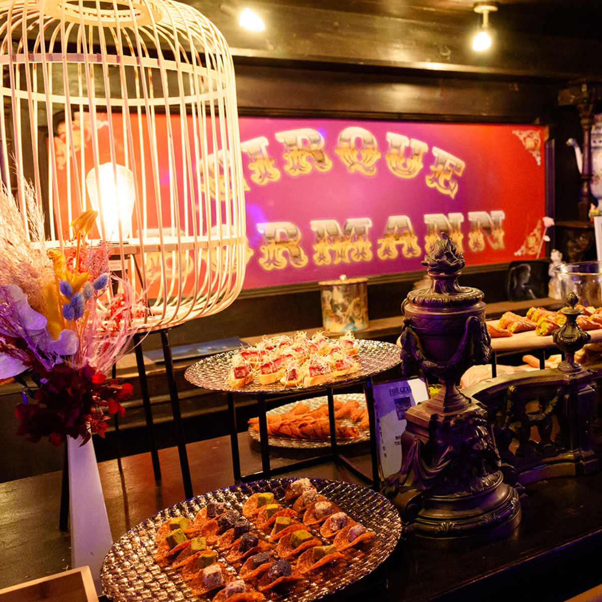 A buffet table displays a variety of appetizers, desserts, and decorative elements under warm lighting in a themed setting.