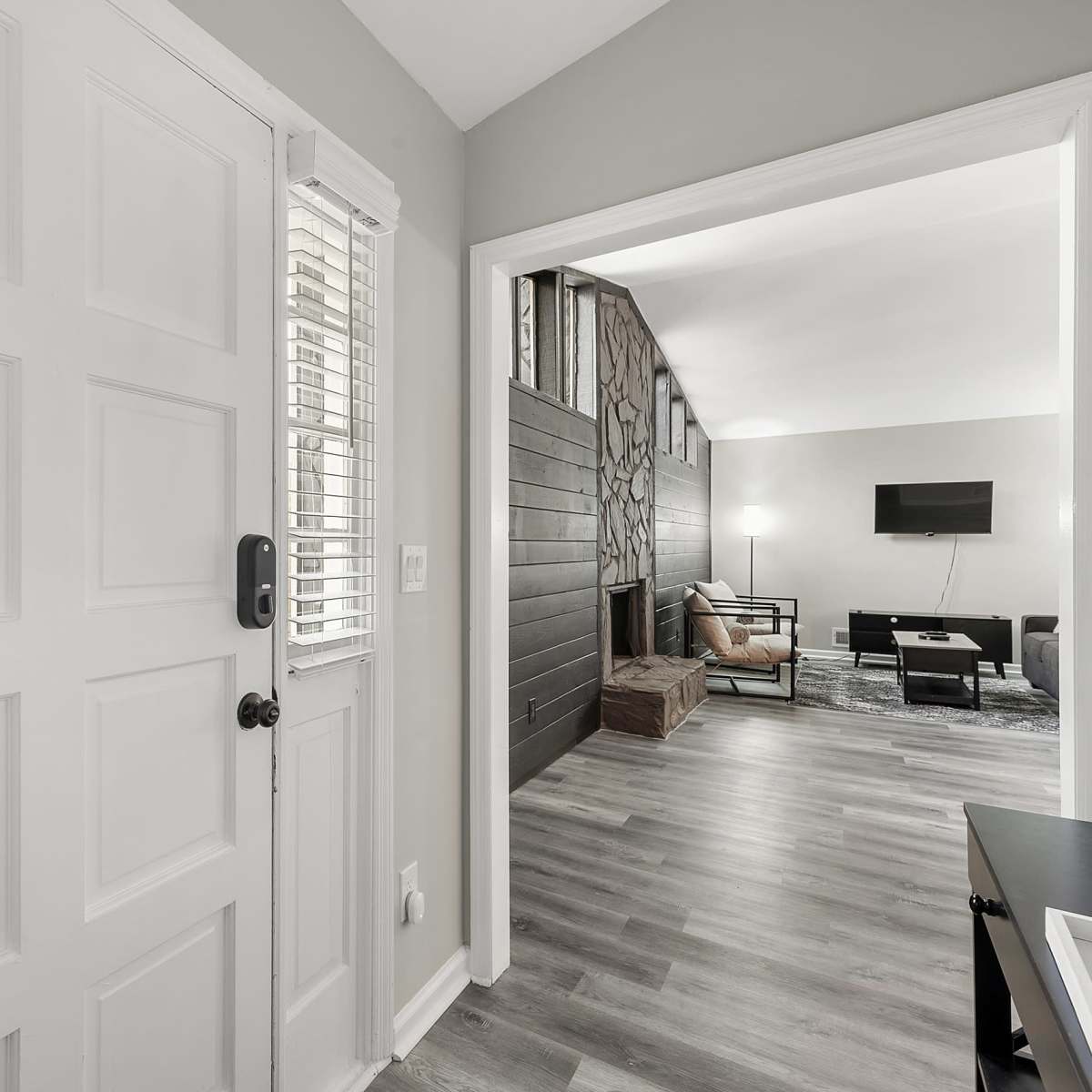 An entryway with a white door and a view into a living room featuring a large window and modern furnishings.