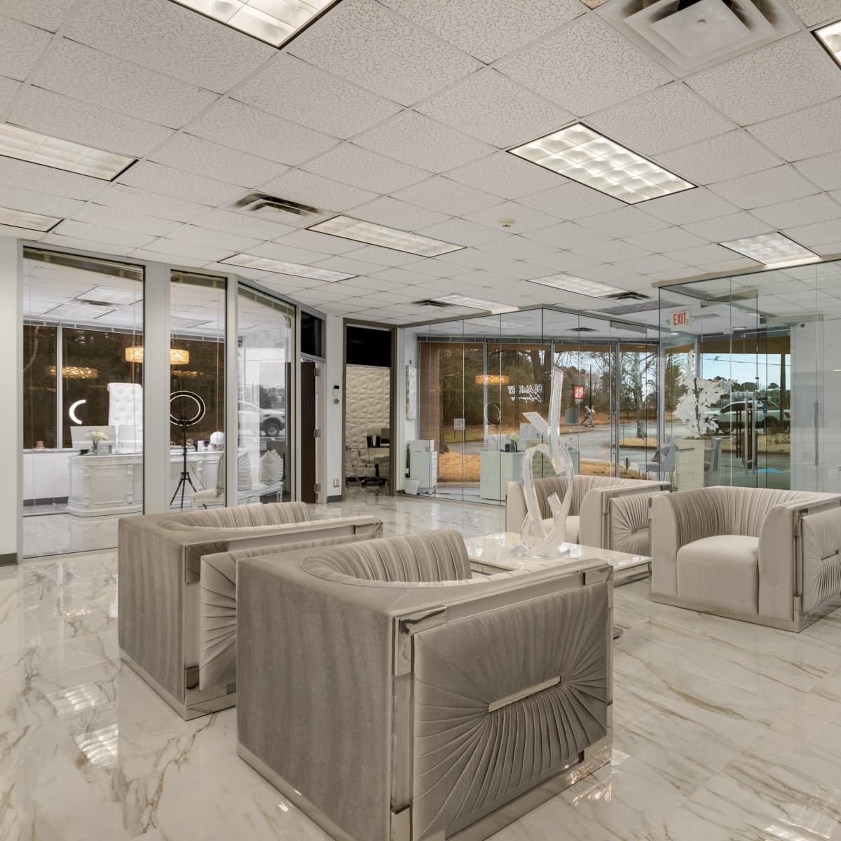 A modern office space with glass walls, marble flooring, and a seating area featuring plush armchairs.