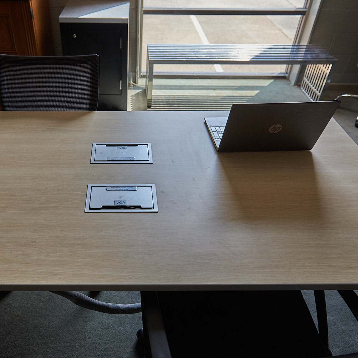 A wooden table with two nameplates and a laptop sits in a well-lit office space.