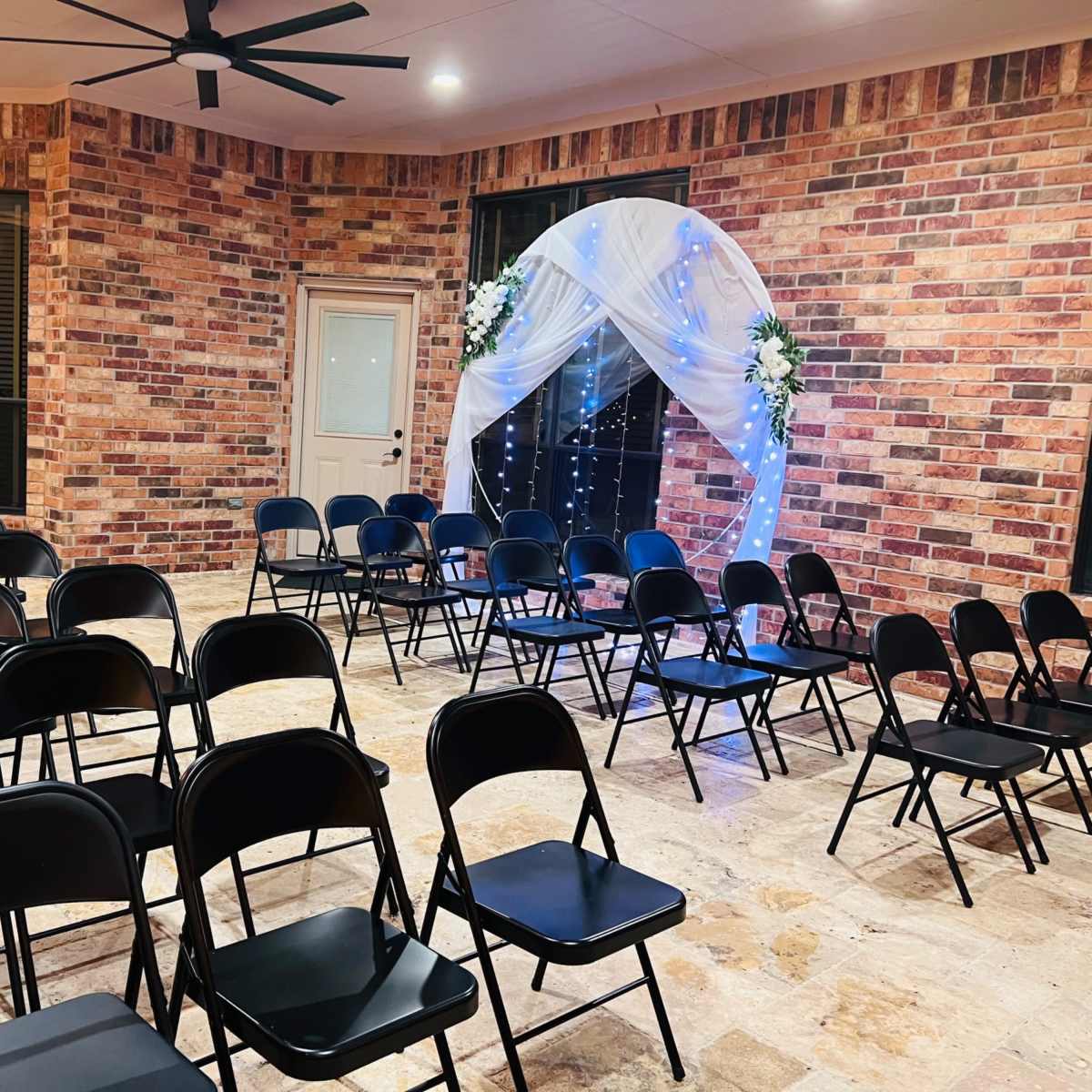 A room with black folding chairs arranged in rows facing a decorated archway draped in white fabric and illuminated by blue lights.