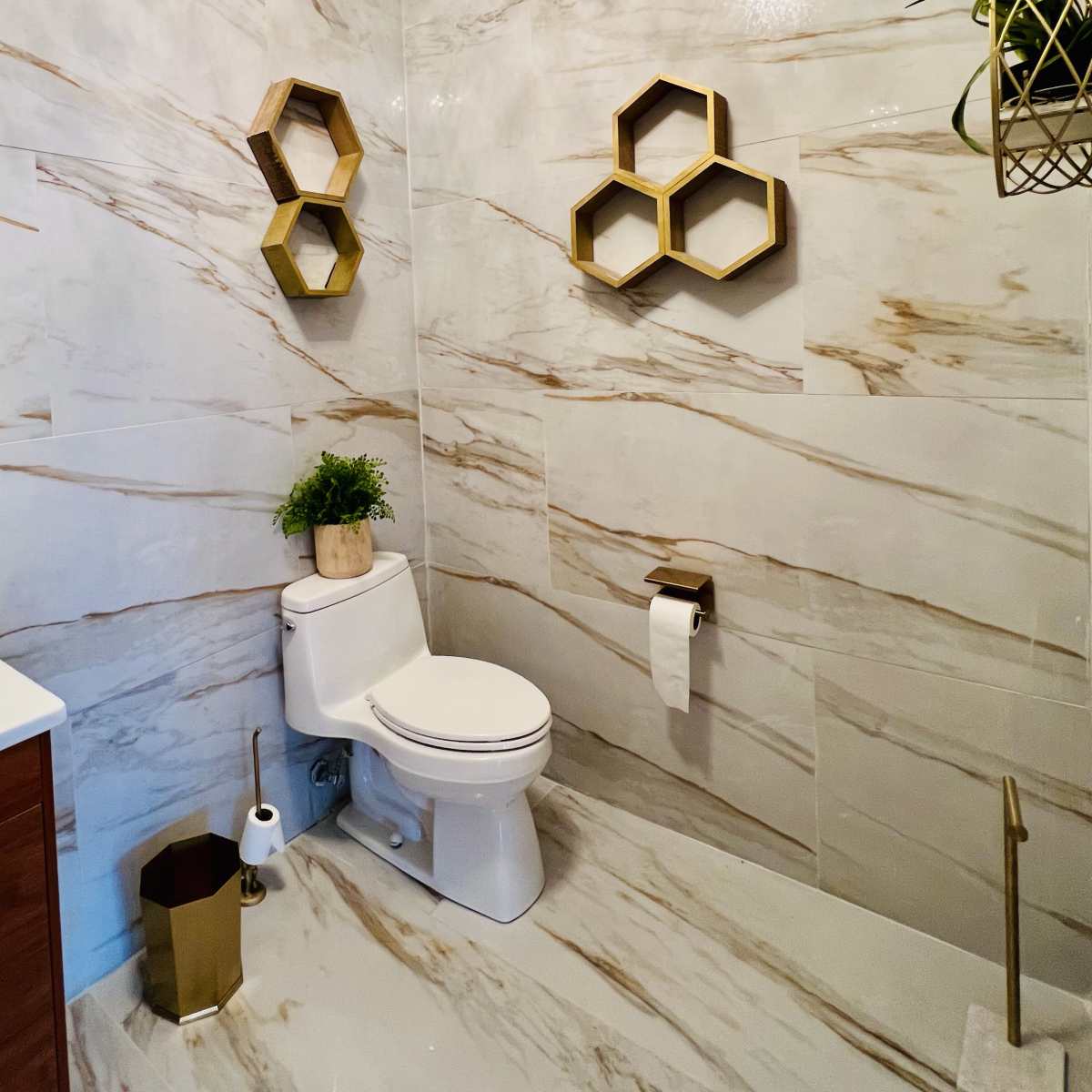 A modern bathroom with marble-patterned walls, a toilet, a sink with wooden cabinetry, and decorative hexagonal shelves.