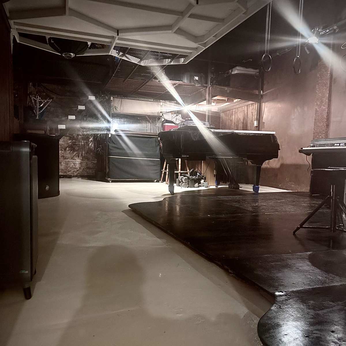 A dimly lit basement space with a smooth floor, dark furniture, and a variety of equipment arranged throughout the area.