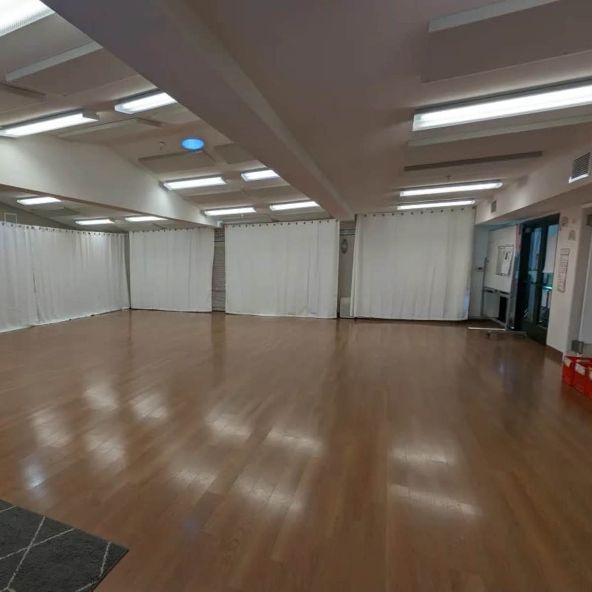 A spacious room with wooden flooring, white curtains dividing the space, and bright overhead lighting.