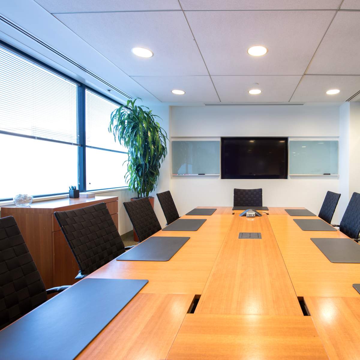 A conference room is set up with a long wooden table, black chairs, and a large screen on the wall.