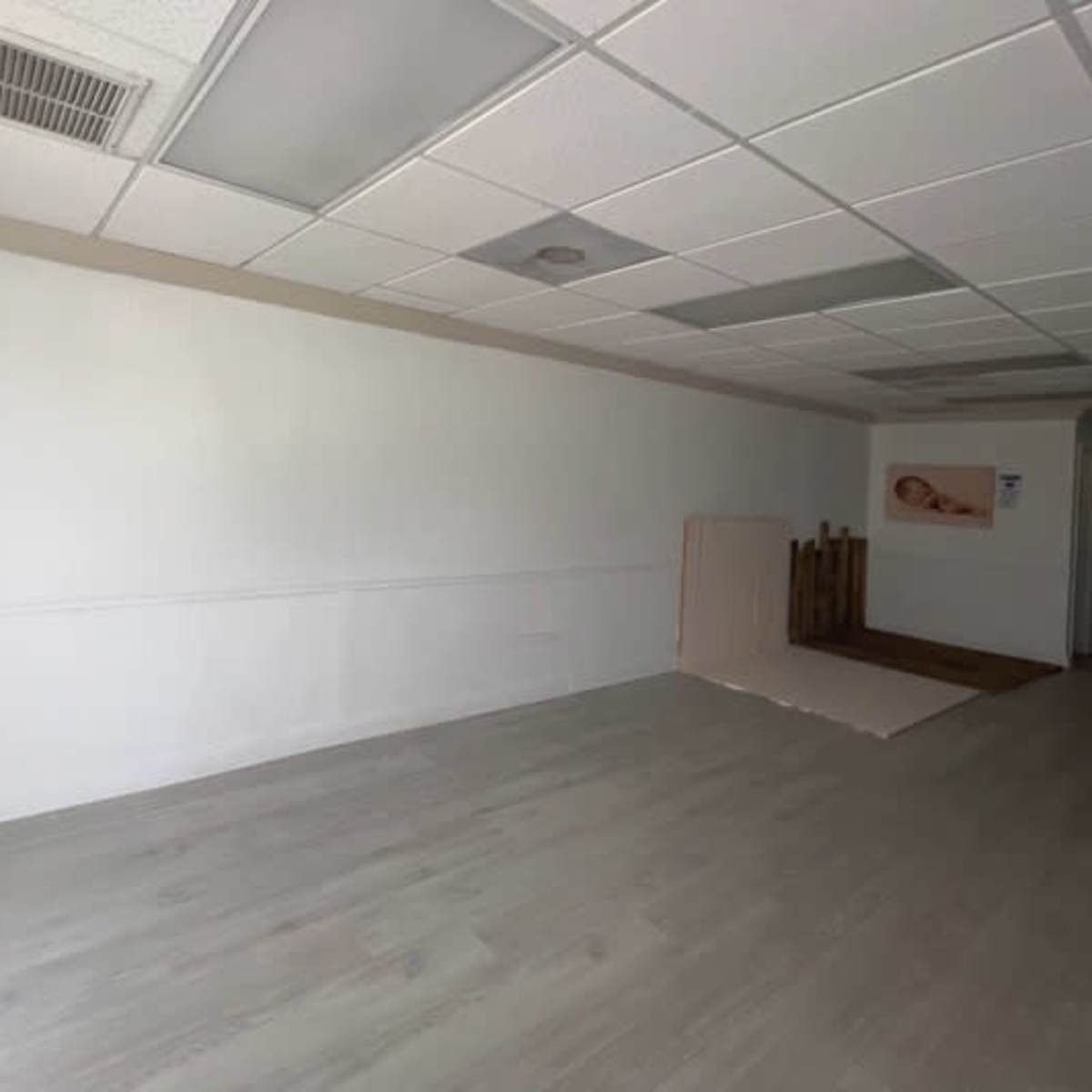 An empty room with a light-colored floor, a white wall on one side, and a wooden structure partially visible at the back.