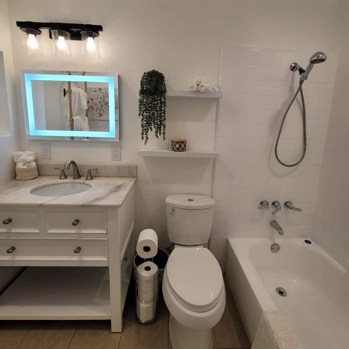 A clean bathroom featuring a sink with cabinetry, a mirror with backlighting, a toilet, a shower with a detachable head, and a bathtub.