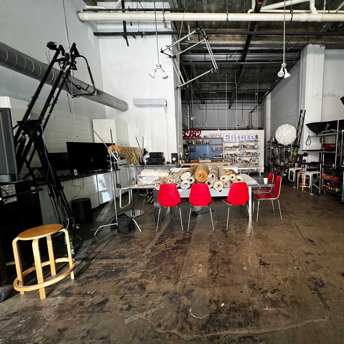 A spacious studio with red chairs arranged around a table, surrounded by various equipment and storage shelves.