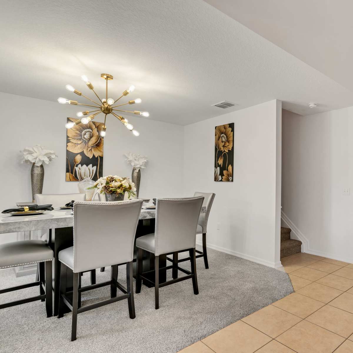 A dining area with a table set for a meal, framed floral wall art, and a welcoming message on the ceiling above.