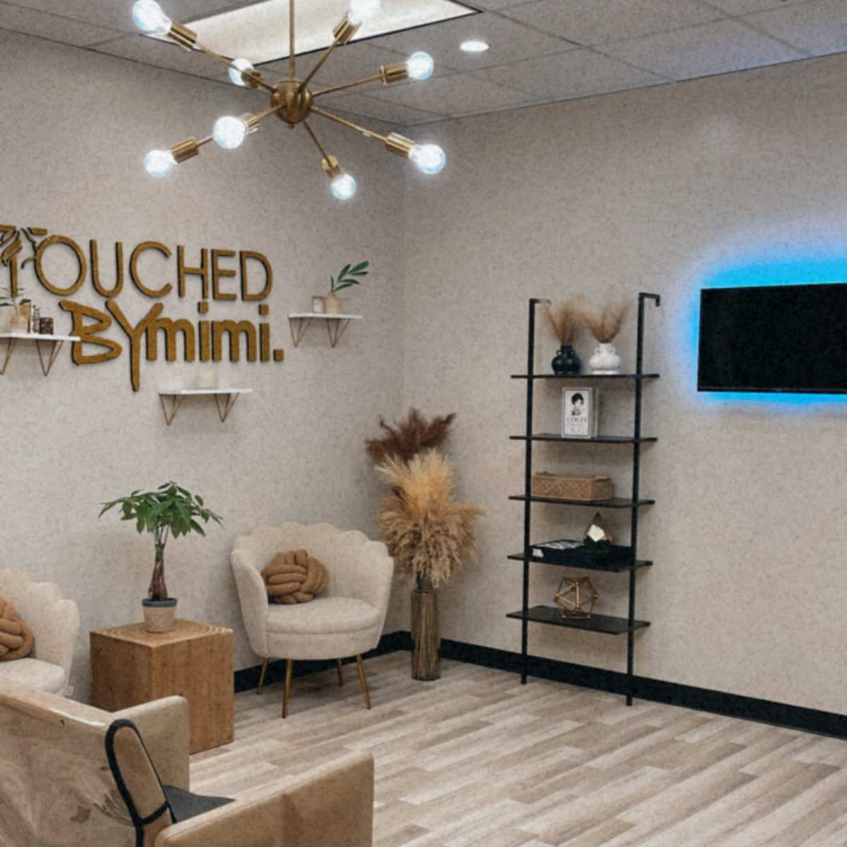A modern salon interior with stylish seating, decorative plants, and a wall sign that reads "TOUCHED BY mimi."