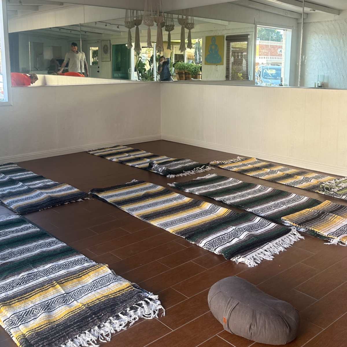 A spacious room with several woven rugs arranged on a tiled floor, a large mirror on one wall, and a few decorative elements in the background.