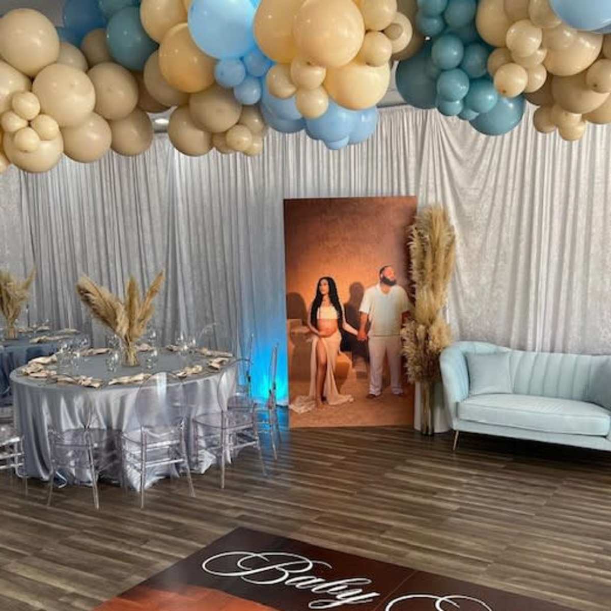 A decorated indoor event space featuring a balloon arch, a table set for dining, and a large photo backdrop of a couple.