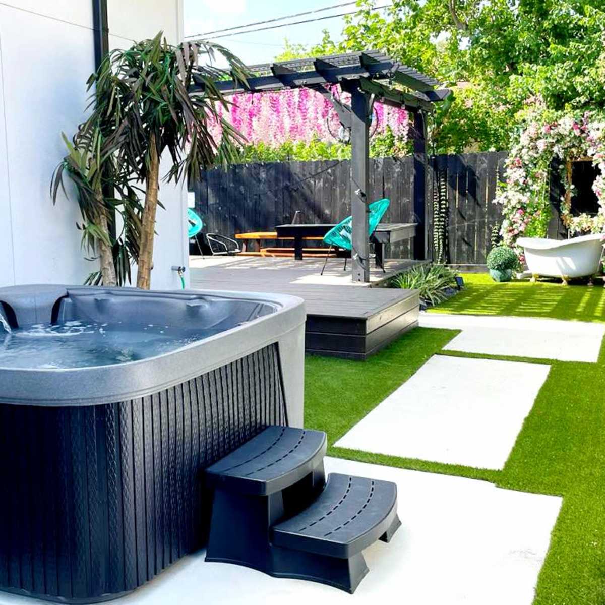 A hot tub sits beside a deck covered with greenery and outdoor seating.