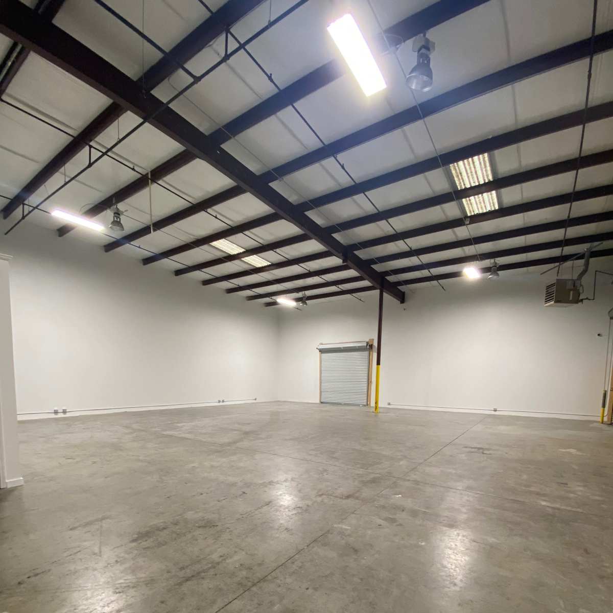 An empty industrial space with a concrete floor, white walls, and exposed metal beams.