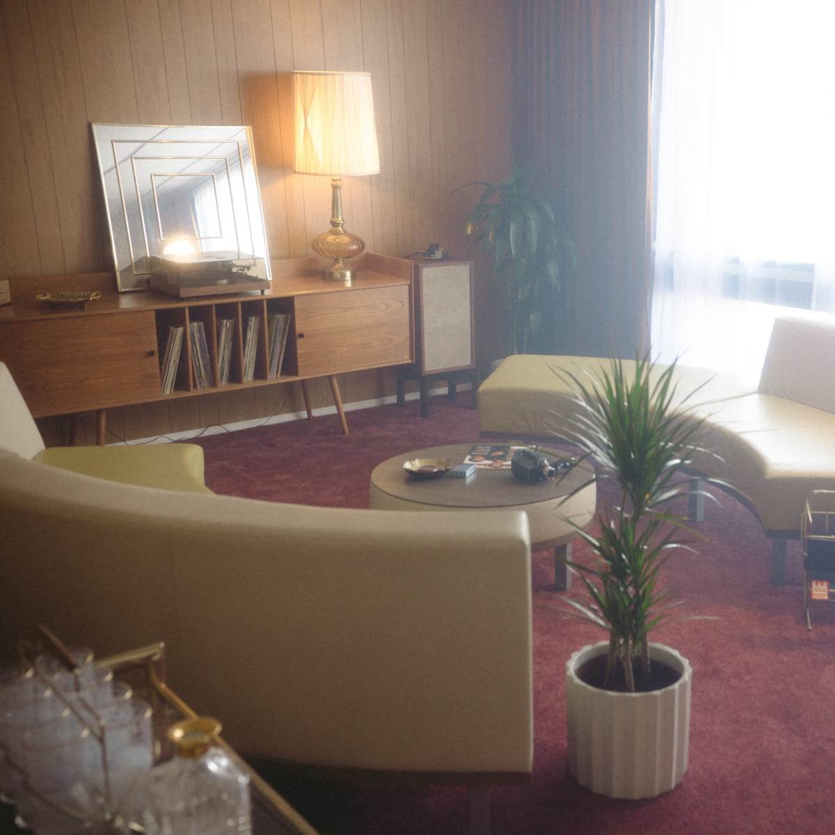 A mid-century modern living room with curved sofas, a round coffee table, and a decorative lamp, all situated on a carpeted floor.