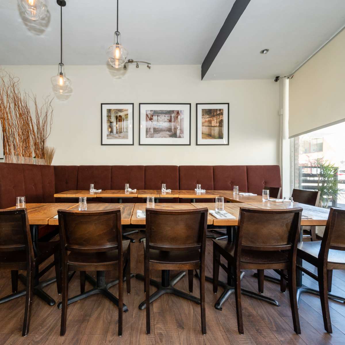 A wooden dining area features a large table surrounded by chairs, with a booth and decorative plants in the background.