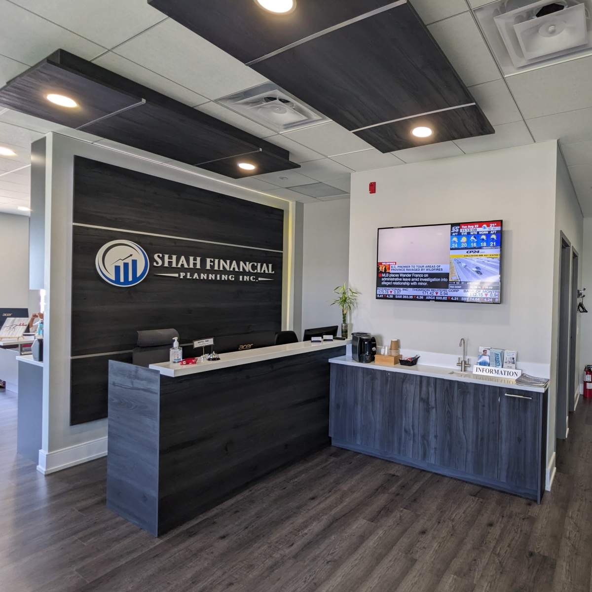 A modern reception area of Shah Financial Planning Inc., featuring a large logo on the wall, a flat-screen TV displaying news, and a sleek reception desk.