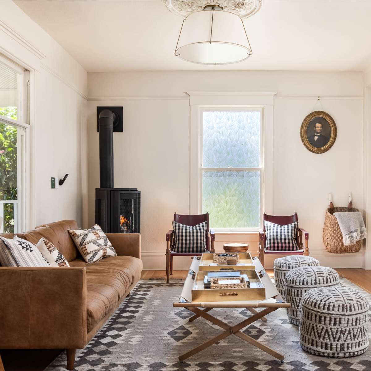The living room features a brown leather sofa, two red chairs, a wooden coffee table, a decorative rug, and a wood-burning stove near a window.
