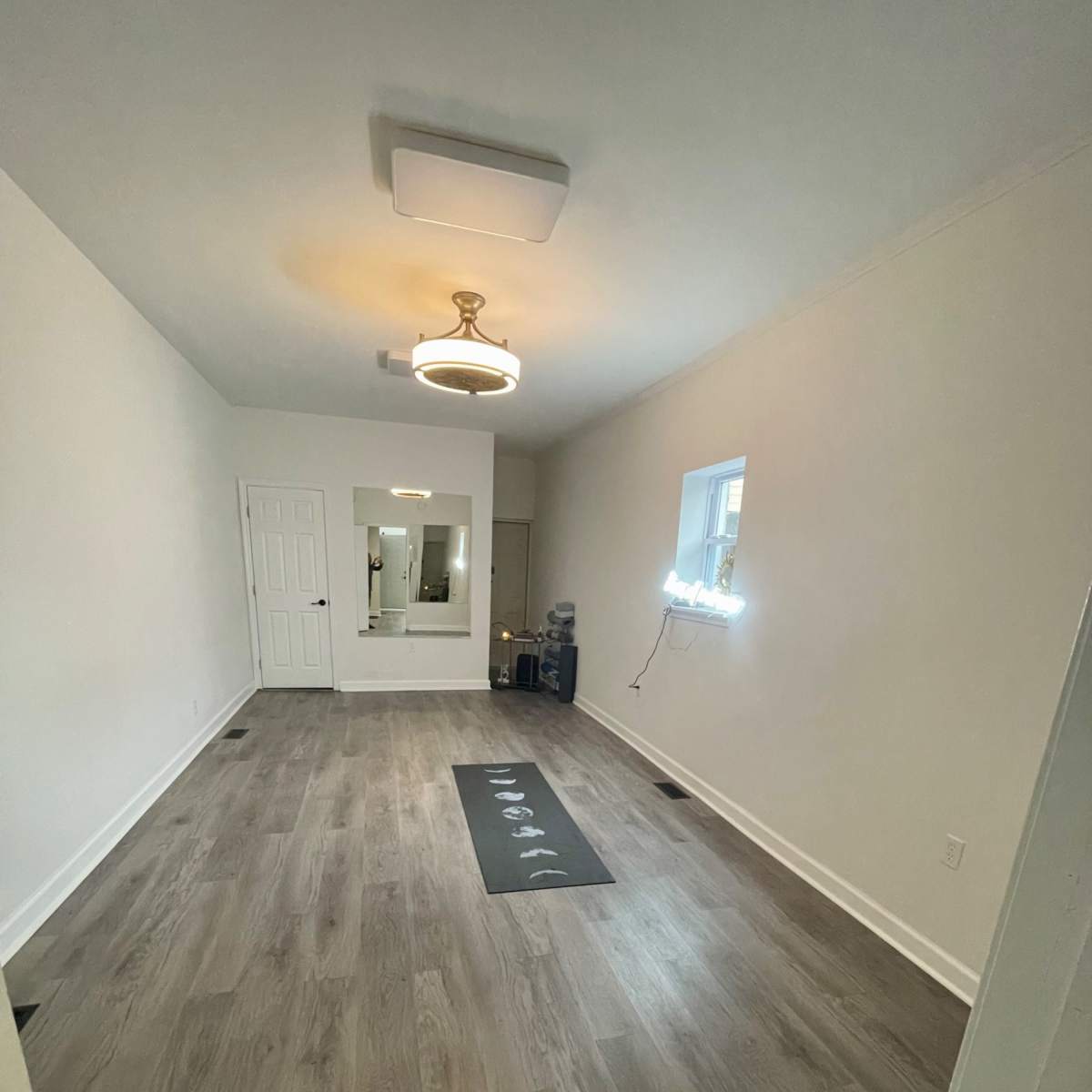 A spacious, empty room with light-colored walls, wooden flooring, and a yoga mat in the center.