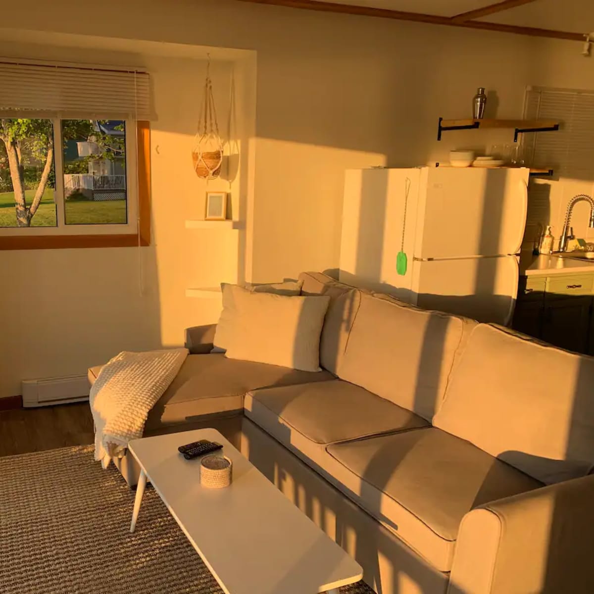 A well-lit living room features a beige sofa, a coffee table, and a window with sunlight streaming in.
