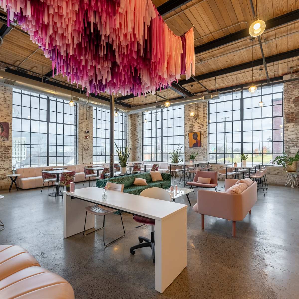The spacious interior of a modern café features large windows, stylish furniture, and a colorful hanging installation.