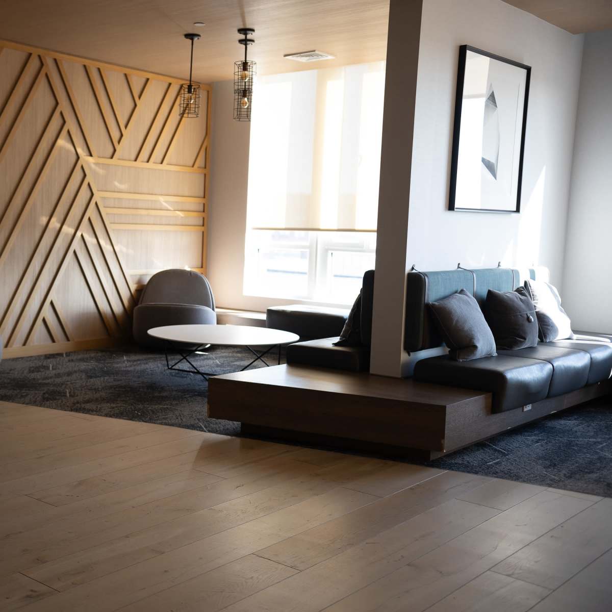 A modern lounge area featuring a wooden accent wall, a black leather sofa, a round coffee table, and several chairs arranged on a wooden floor.