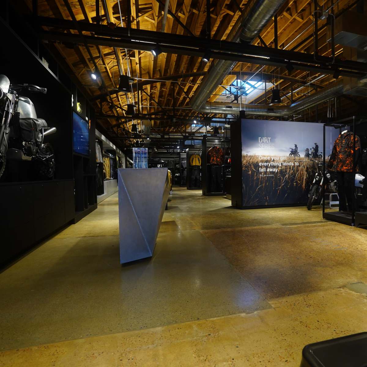 A spacious retail store interior with displays of clothing and gear, featuring a wooden beamed ceiling and industrial-style elements.