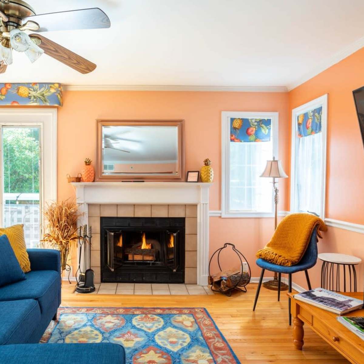 The living room features a blue sofa, a fireplace with a mantel, and large windows surrounded by orange walls.