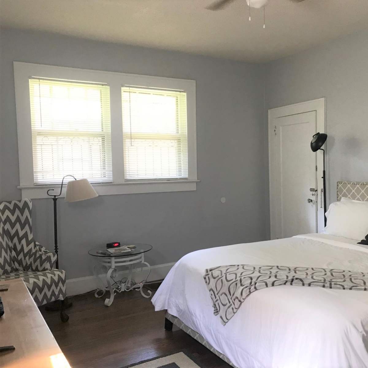 A bedroom with a bed, a chair, a small side table, and a piece of artwork featuring a heart on the wall.