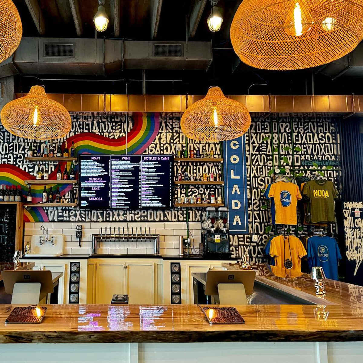 A bar with a wooden counter, a vibrant mural on the wall, and decorative hanging light fixtures.