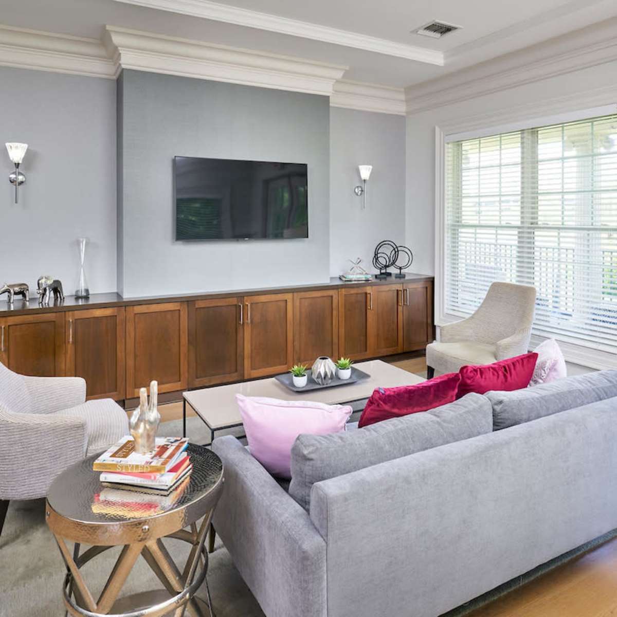 A modern living room with a gray sofa, two chairs, a round side table, and a mounted television above a wooden cabinet.
