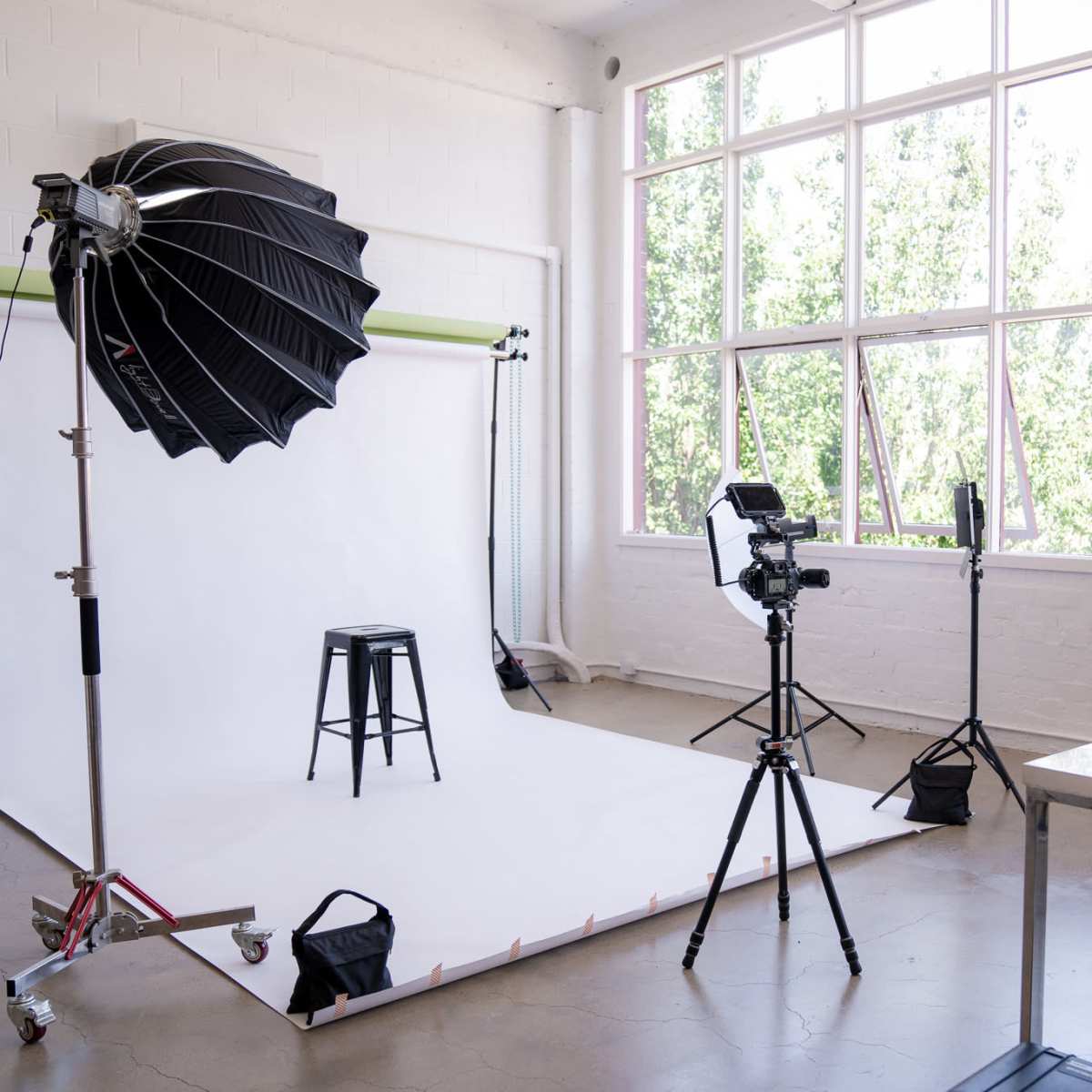 A photography studio setup with a white backdrop, a stool, various lighting equipment, and a camera on a tripod.