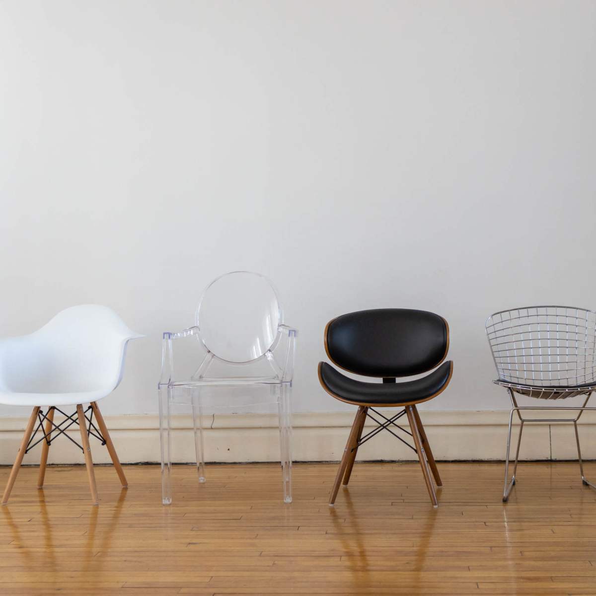 Five distinct chairs lined up against a plain wall, showcasing a variety of designs and materials.