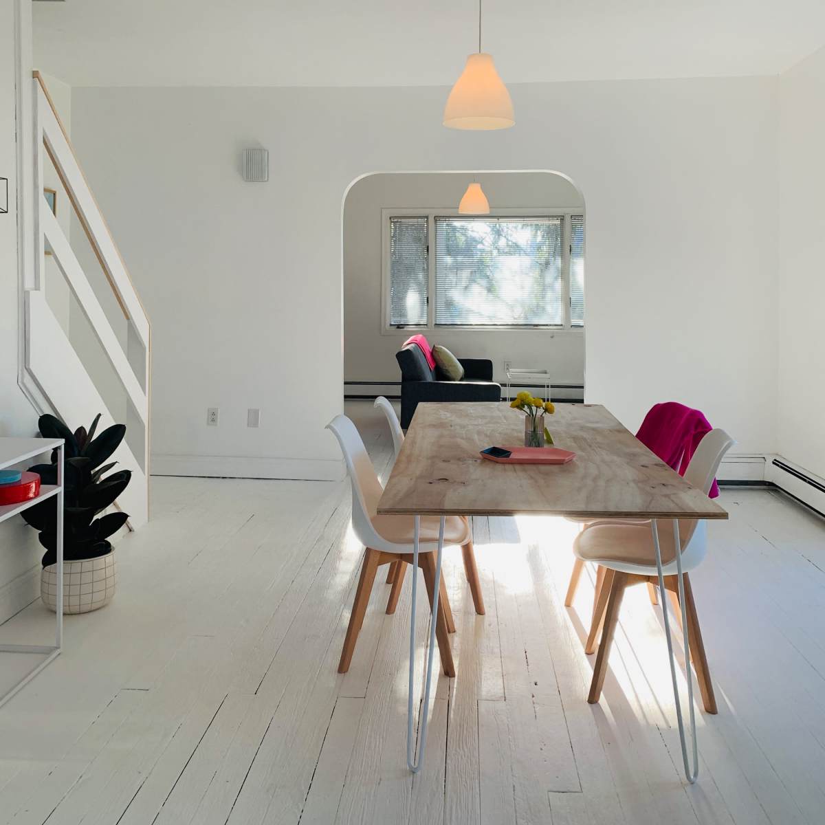 A bright dining area features a wooden table surrounded by white chairs, with a staircase visible in the background and a couch in a cozy corner.
