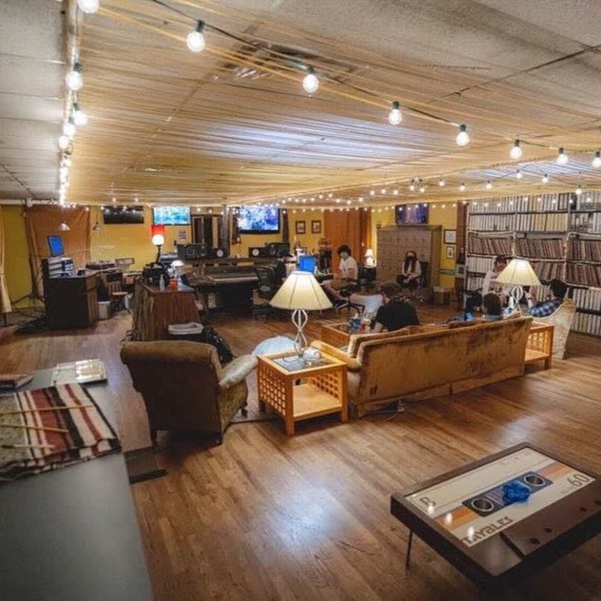 A spacious, well-lit lounge area with several couches, tables, and screens, where people are seated and engaging in various activities.