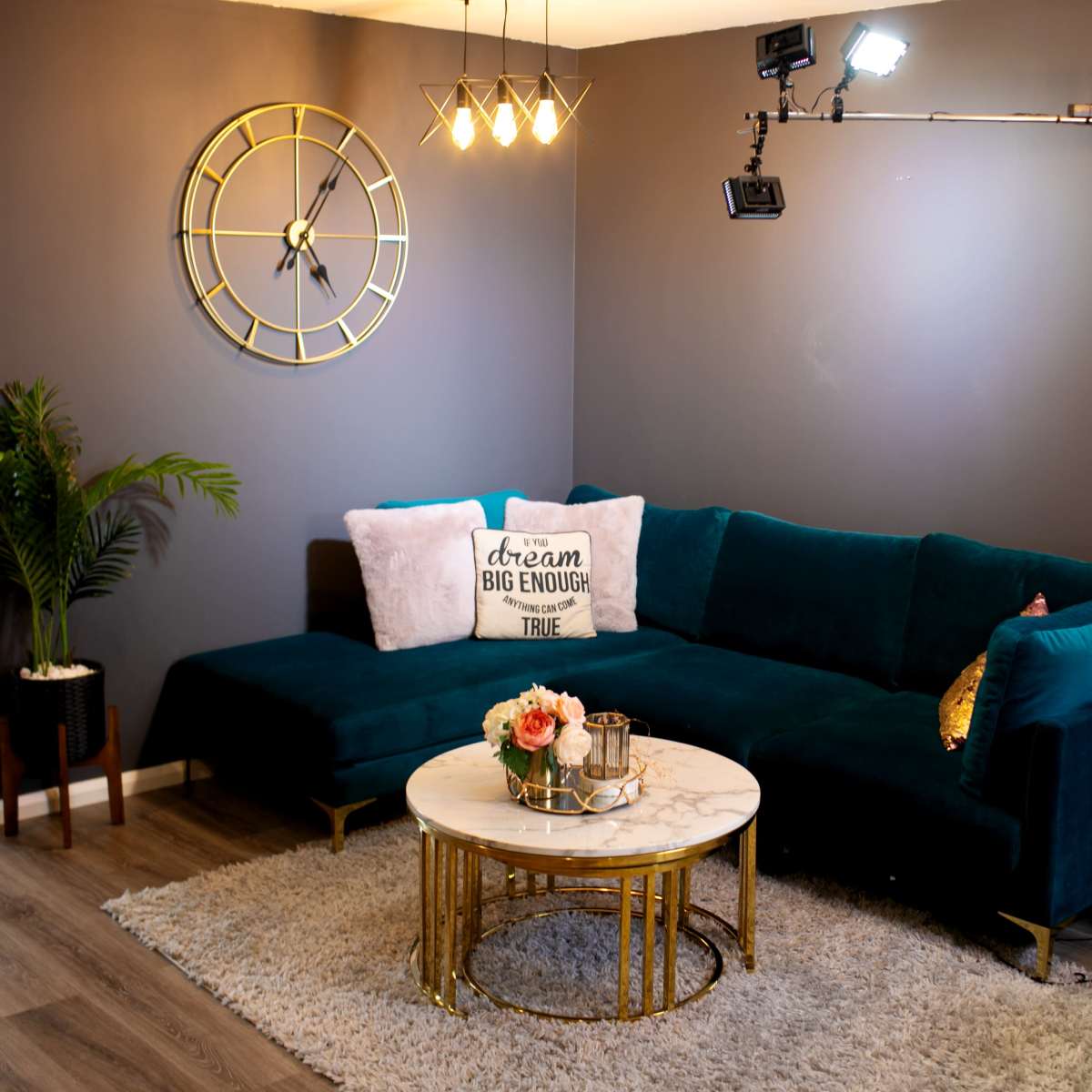 A cozy living room featuring a dark green sectional sofa, a round marble coffee table, and decorative elements like a clock and potted plants against a gray wall.