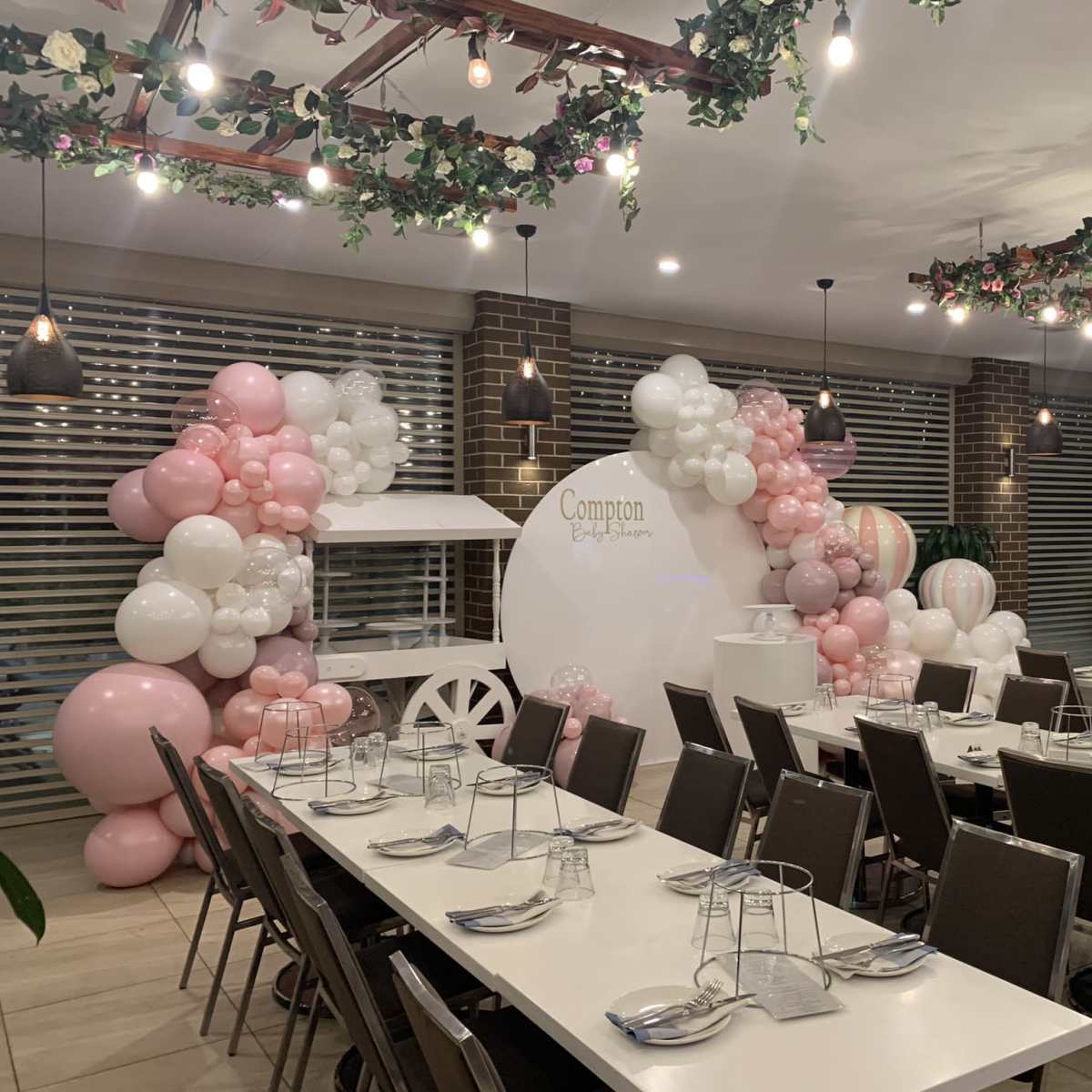 A banquet room is decorated with balloons in pink and white, featuring a carriage display and set with long tables for dining.