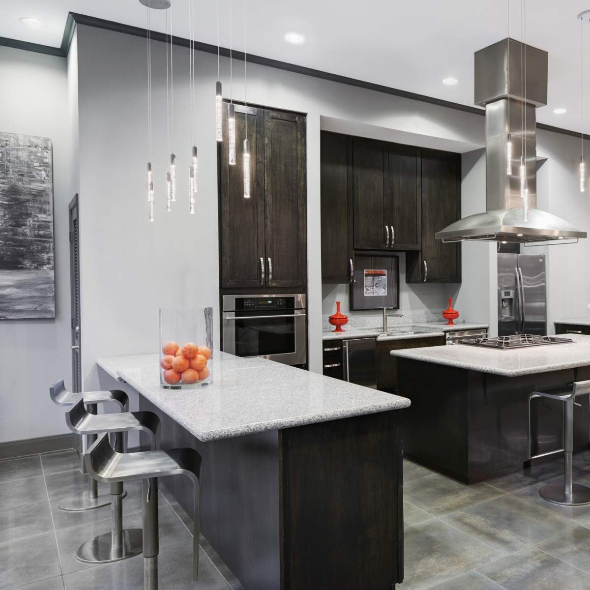 A modern kitchen features dark cabinetry, a central island with a gray countertop, and stainless steel appliances, illuminated by pendant lights.