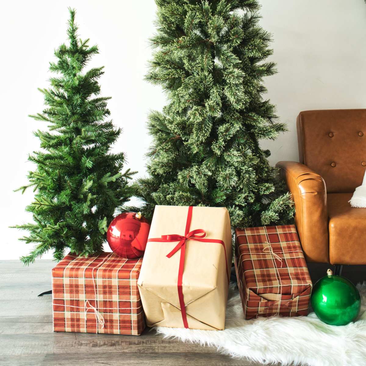 The scene features two Christmas trees beside a brown leather chair, with wrapped presents and ornaments arranged neatly on the floor.