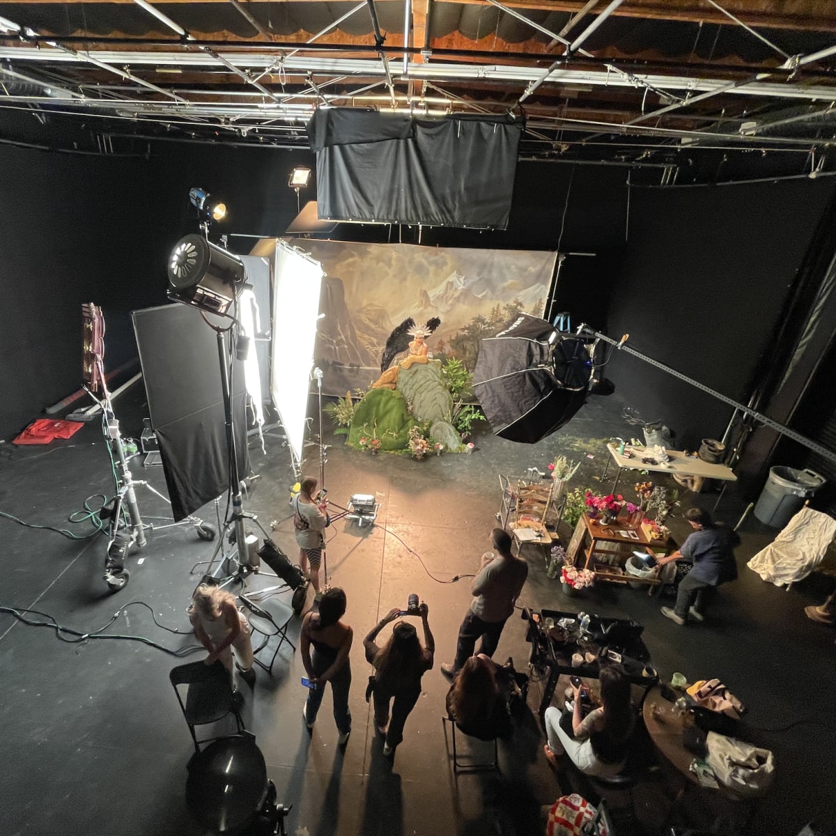 A film set is arranged with lighting equipment and a backdrop, where a group of people is preparing for a shoot.